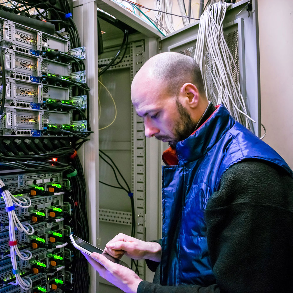 A man with a digital tablet working in a server room.